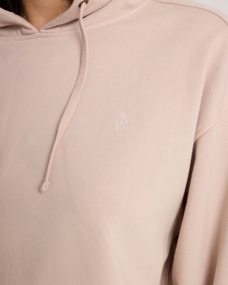 A person wearing the Volcom Women’s Stone Soft Hoodie in light pink, made from a soft cotton-blend fleece and featuring a small embroidered logo on the chest. Only part of the upper body is visible.