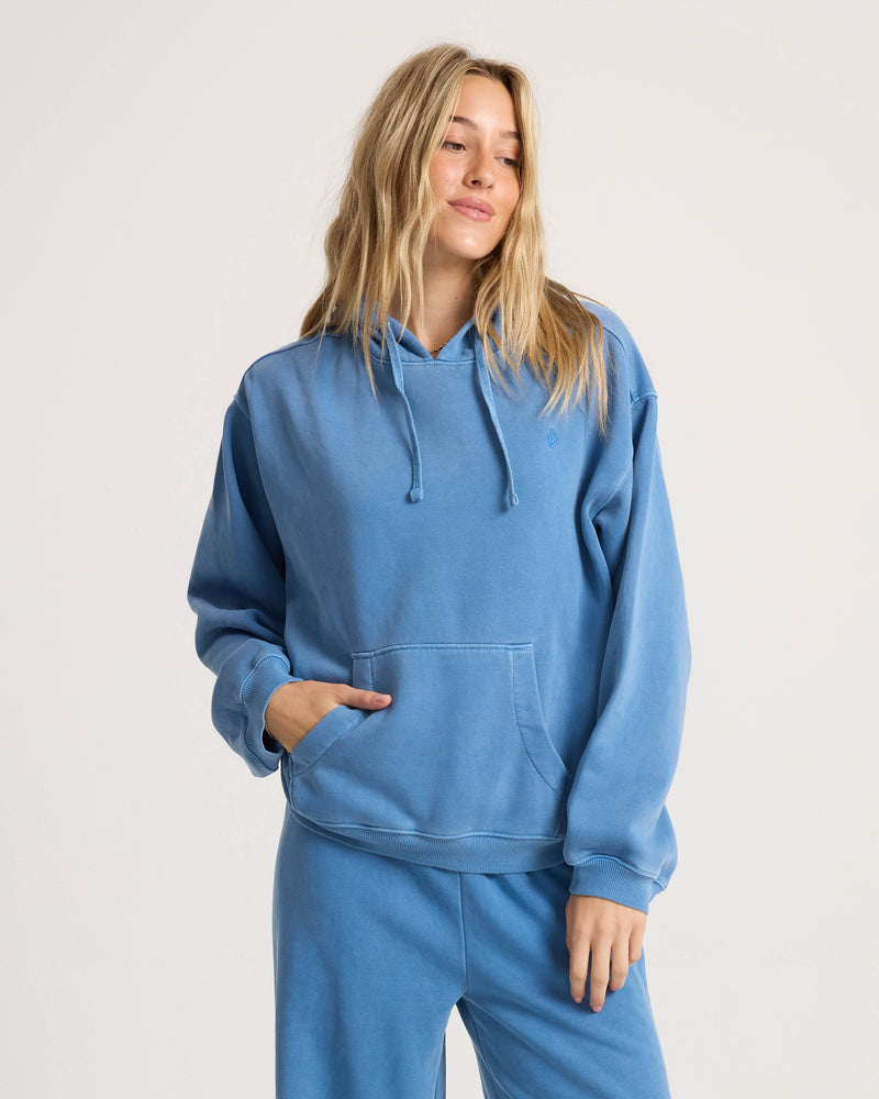 A person wearing a blue Volcom Women’s Stone Soft Hoodie, a relaxed fit fleece with a front kangaroo pocket.