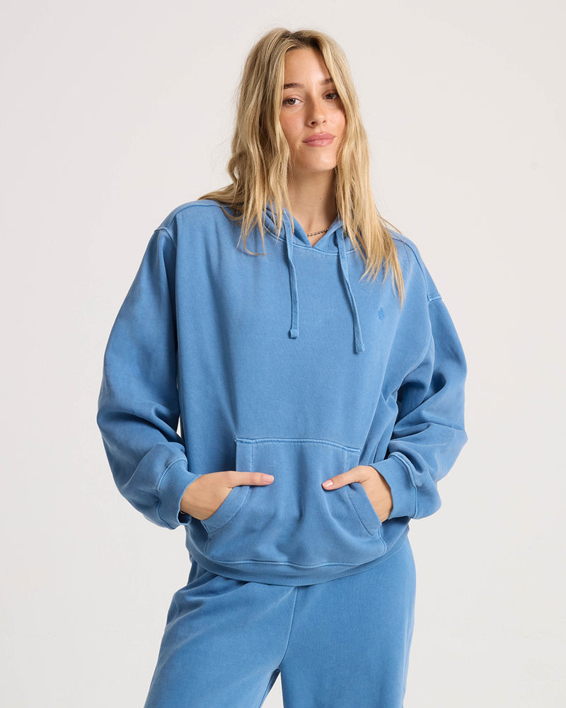 A person wearing a relaxed-fit blue Volcom Women’s Stone Soft Hoodie with a front kangaroo pocket.