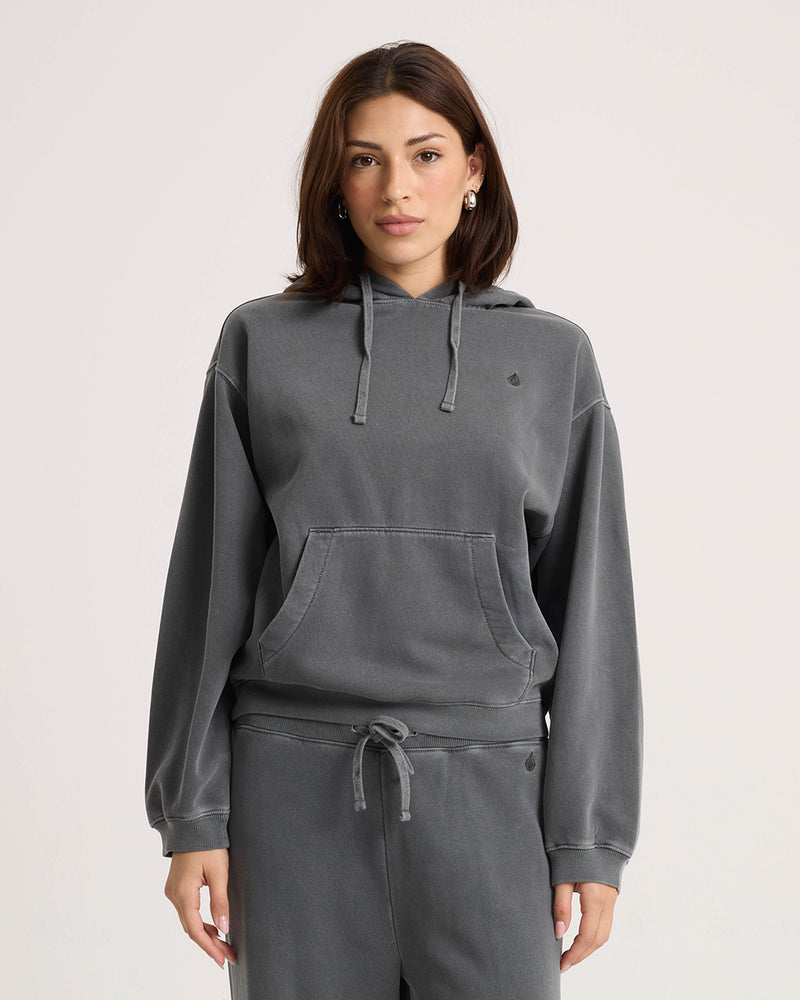A person wearing a relaxed, vintage black Women’s Stone Soft Hoodie with a front kangaroo pocket and matching drawstring sweatpants.