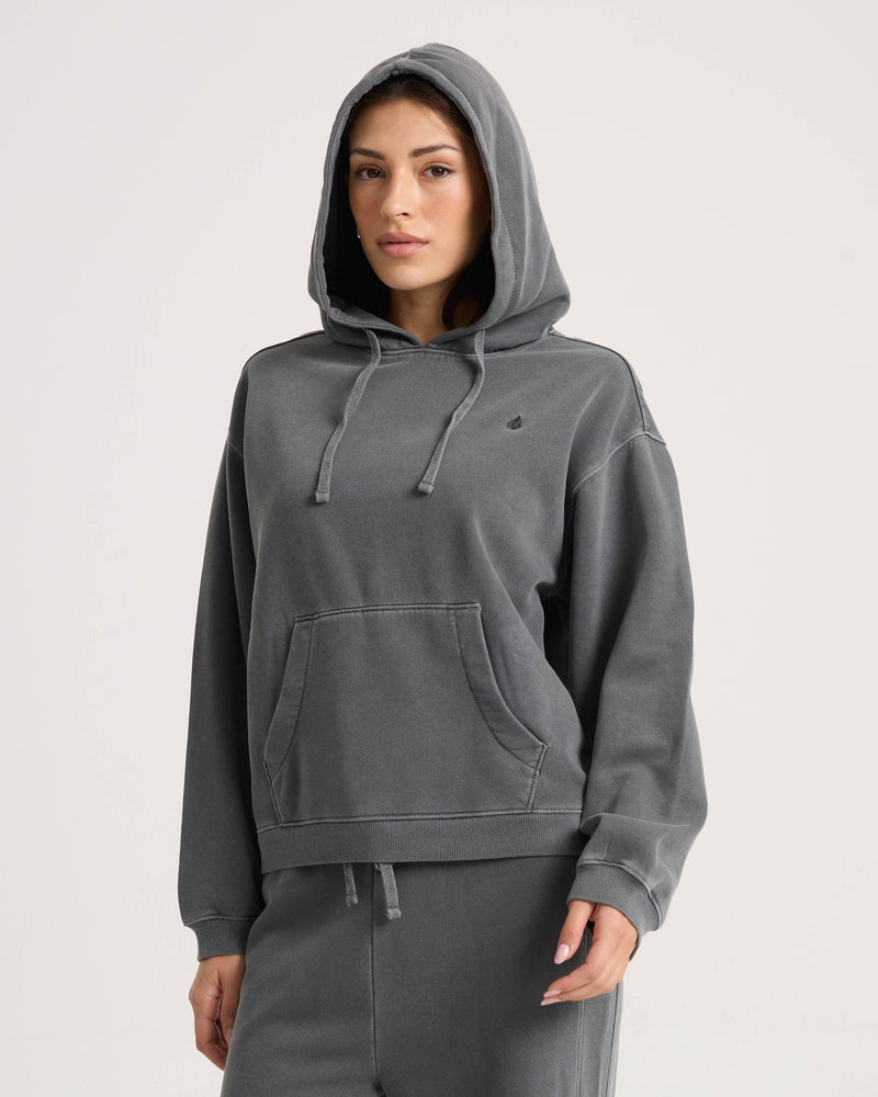 A woman wearing a Volcom Women’s Stone Soft Hoodie, a vintage black, plush fleece pullover with a front kangaroo pocket and an adjustable drawstring hood.