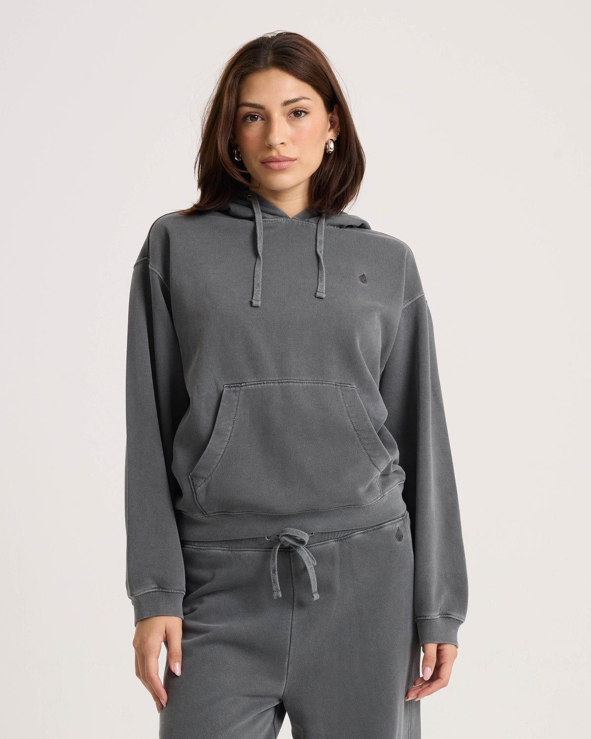 A woman wearing a black, relaxed Volcom Women’s Stone Soft Hoodie with a front kangaroo pocket and drawstring.