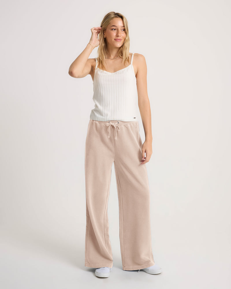 Woman wearing a white ribbed camisole and Volcom Women’s Stone Soft Pants in khaki, featuring a loose-fit, pull-on design with a drawstring waist.