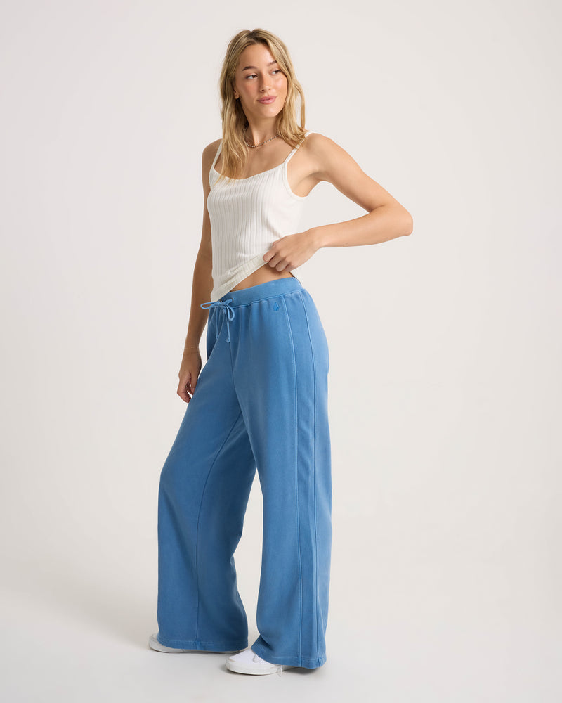 A person wearing a white ribbed tank top and Volcom Women’s Stone Soft Pant, which are wide-leg blue sweatpants with a tie-front waist.
