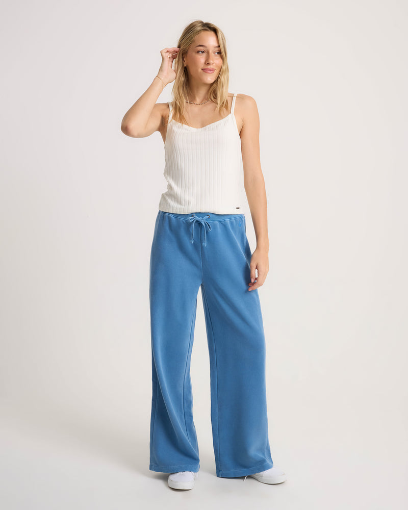 A woman wearing a white ribbed camisole and blue Women’s Stone Soft Pant with a loose-fit, tie-front waist.
