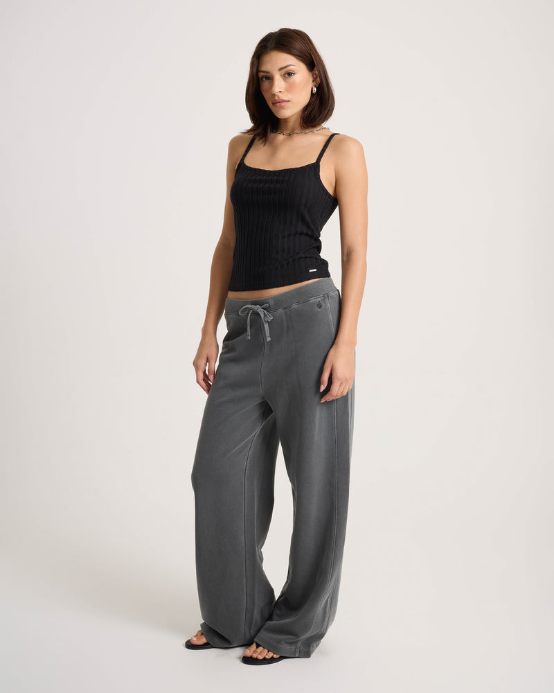 A woman wearing a black sleeveless top and Volcom Women’s Stone Soft Pants in a relaxed fit cotton-blend knit stands against a plain white background, looking at the camera with a neutral expression.