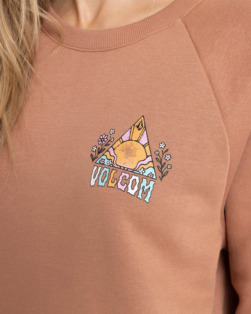A close-up of the Volcom Women’s Stone Magic Bf sweatshirt in a cozy Mocha Mousse color, crafted from soft fleece with a crew neck and decorated with a graphic of a sun, mountains, flowers, and colorful block letters spelling out VOLCOM.