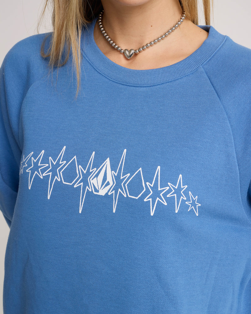 Wearing the Volcom Women’s Stone Magic Bf sweatshirt—a relaxed fit fleece in riverside blue with a white star pattern and a small geometric logo—this look is styled with a silver beaded heart pendant necklace.
