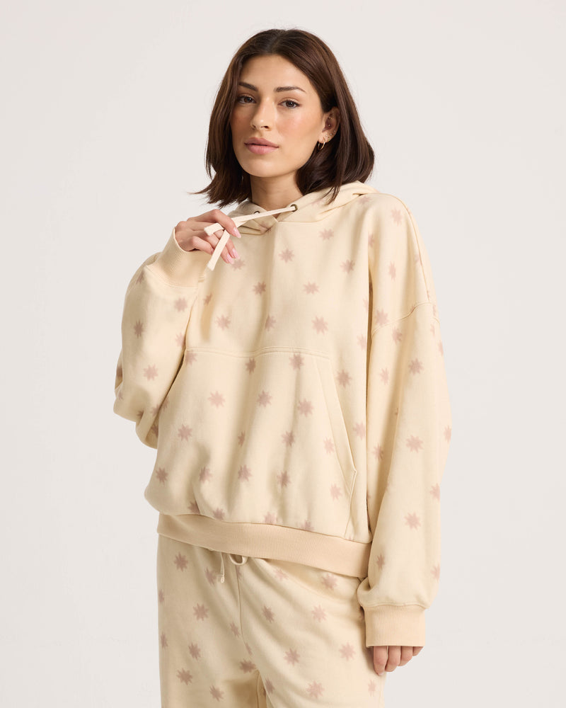 A woman models the Volcom Women’s In A Cinch Sweatshirt—beige with a light star pattern—against a white background, highlighting its relaxed fit and soft fleece material.