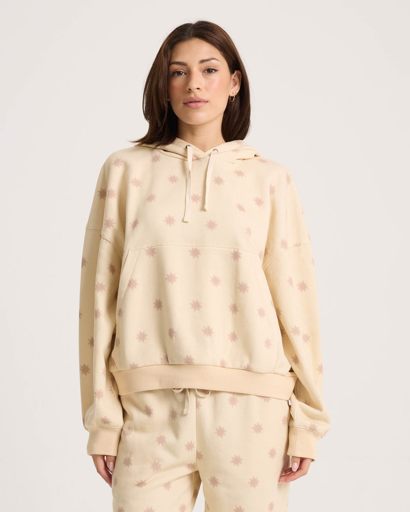 A woman wearing the Women’s In A Cinch Sweatshirt by Volcom—an oversized beige pullover with matching star-patterned sweatpants, made from soft fleece for a relaxed fit—stands against a plain white background.