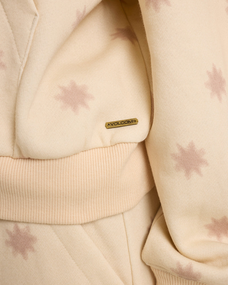 Close-up of the Women’s In A Cinch Sweatshirt by Volcom: relaxed fit, cream fabric with light pink stars, ribbed waistband, and a small metallic Volcom label attached.