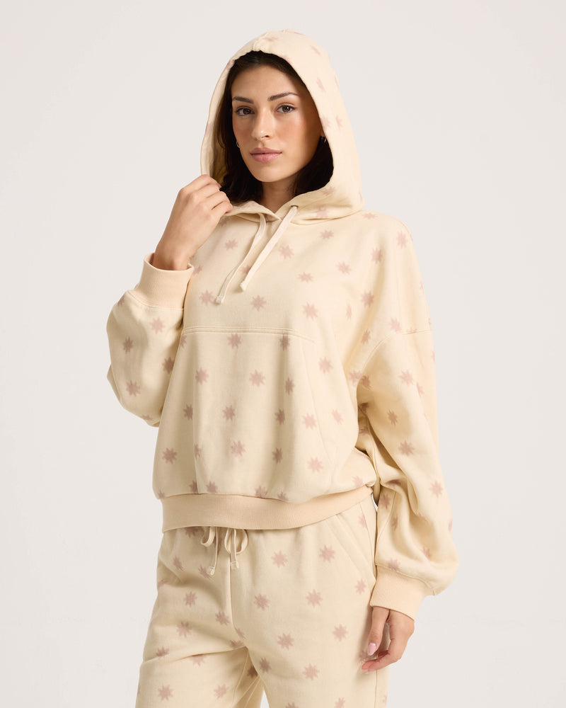 A woman wears the Volcom Women’s In A Cinch Sweatshirt in cream, paired with light pink star-print sweatpants, standing against a plain white background and looking at the camera.