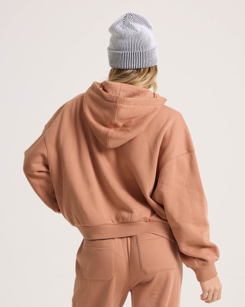A person is seen from behind wearing the Volcom Women’s In A Cinch Sweatshirt in peach, matching sweatpants, and a white and gray striped beanie.