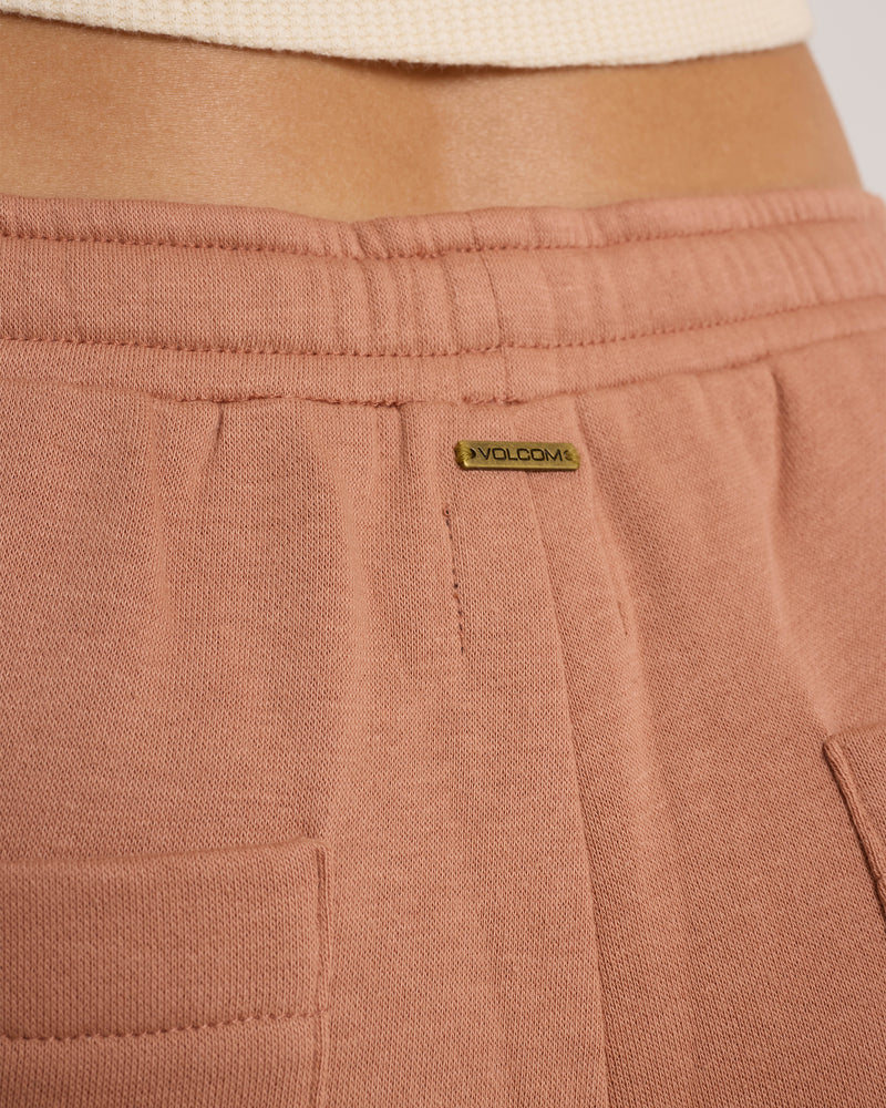Close-up of a person’s waist in Women’s In A Cinch Jogger Pant by Volcom—ribbed mauve sweatpants with an elastic waistband and logo tag for all-day comfort. The top of a cream ribbed shirt peeks out.