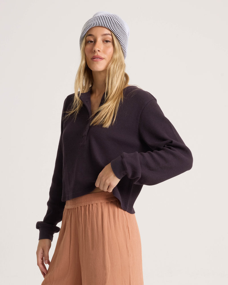 A woman wears a long-sleeved Volcom Women’s Ski Bum Henley and a striped beanie.