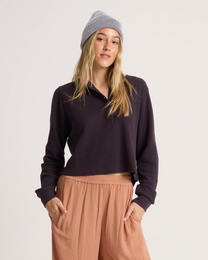 A person wearing a Volcom Women’s Ski Bum Henley, peach-colored pants, and a black-and-white striped beanie.