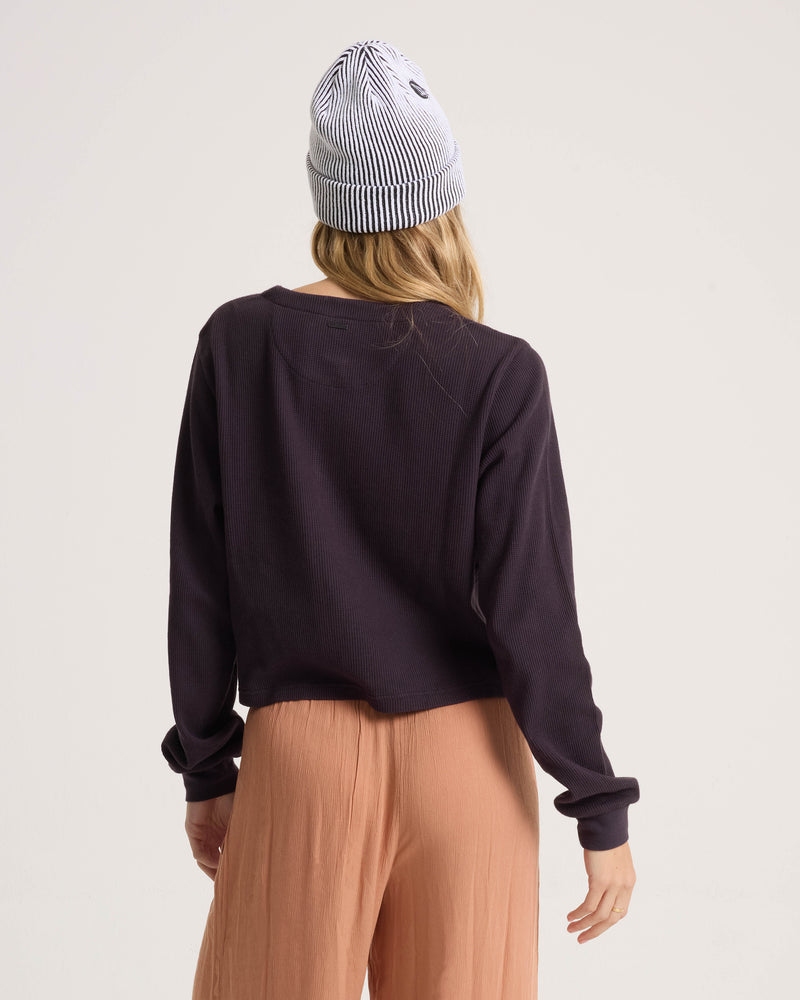 Back view of a person wearing a Volcom Women’s Ski Bum Henley, tan wide-leg trousers, and a black-and-white striped beanie.