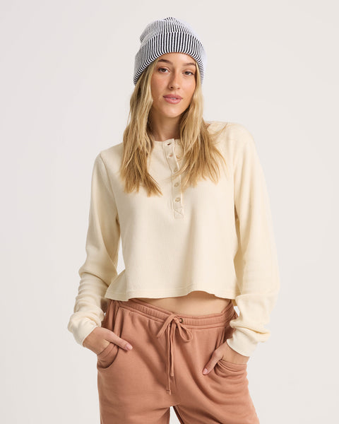 Woman wearing a cream-colored cotton Women’s Ski Bum Henley by Volcom and a black-and-white striped beanie.