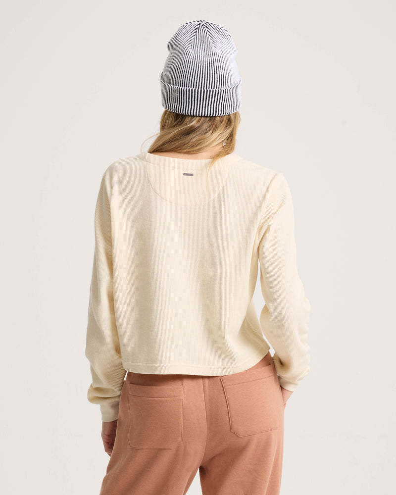 Back view of a person wearing a cream-colored cotton Women’s Ski Bum Henley by Volcom and a black and white striped beanie.