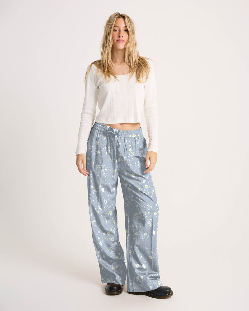 A person wearing a white long-sleeved shirt and Volcom Women’s Longboard Wide Leg Pant in a lightweight white daisy print.