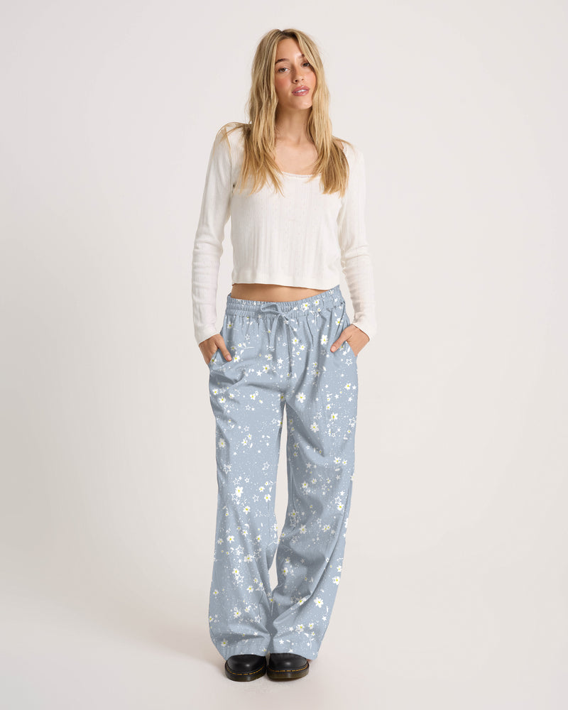 A person wearing a white long-sleeve top and Volcom Women’s Longboard Wide Leg Pant in light blue with a white daisy pattern.