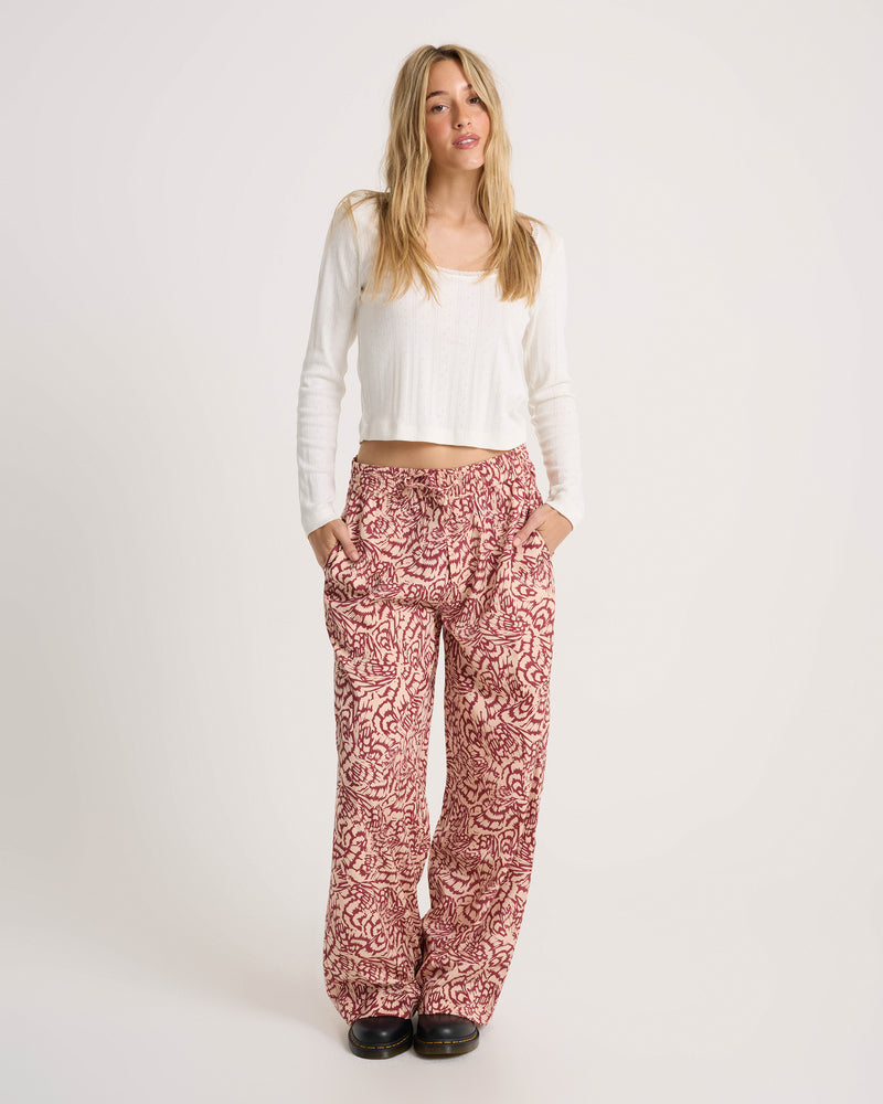 A woman wearing a white long-sleeved top and Volcom Women’s Longboard Wide Leg Pant with a relaxed, drawstring fit, standing with her hands in her pockets.