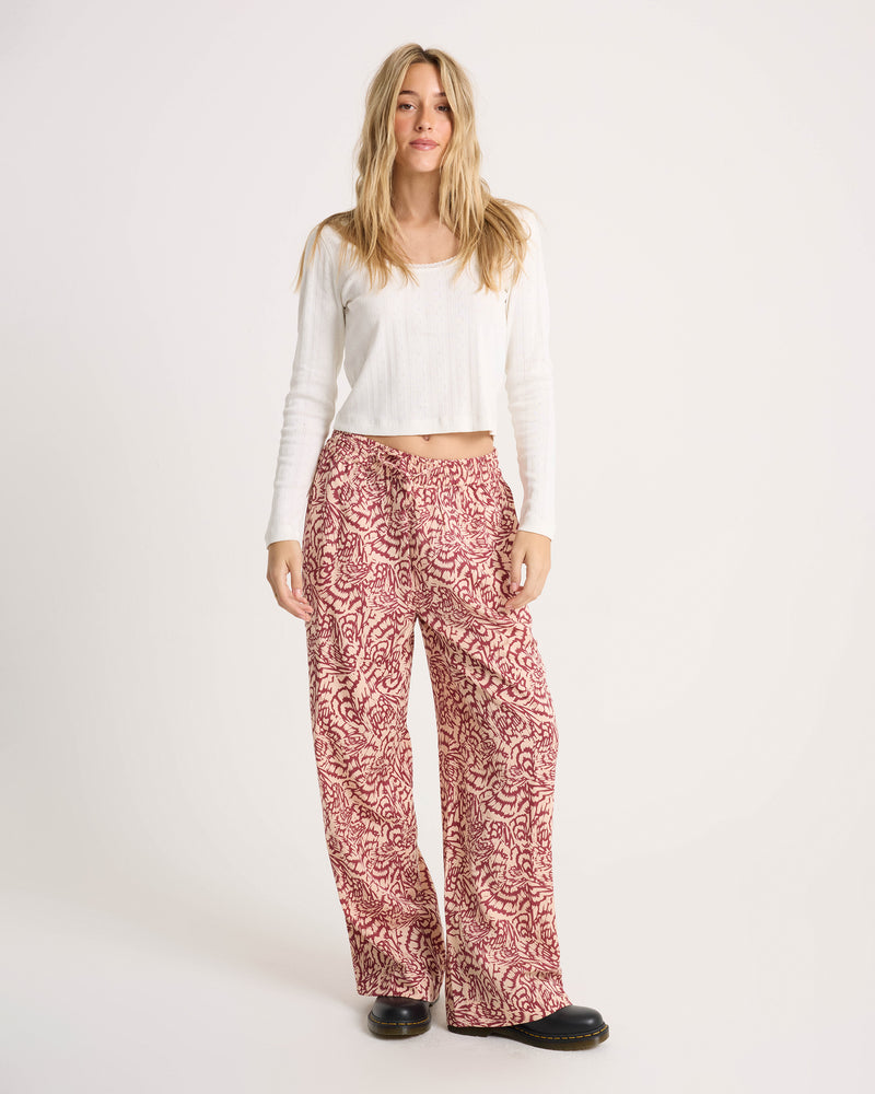 A woman wears a white long-sleeved top and patterned Women’s Longboard Wide Leg Pant.