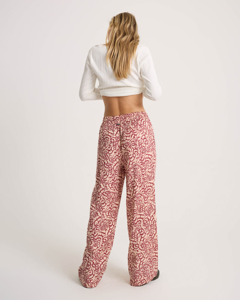 A woman seen from behind, wearing a white long-sleeve crop top and Volcom Women’s Longboard Wide Leg Pant in a red and cream abstract print.