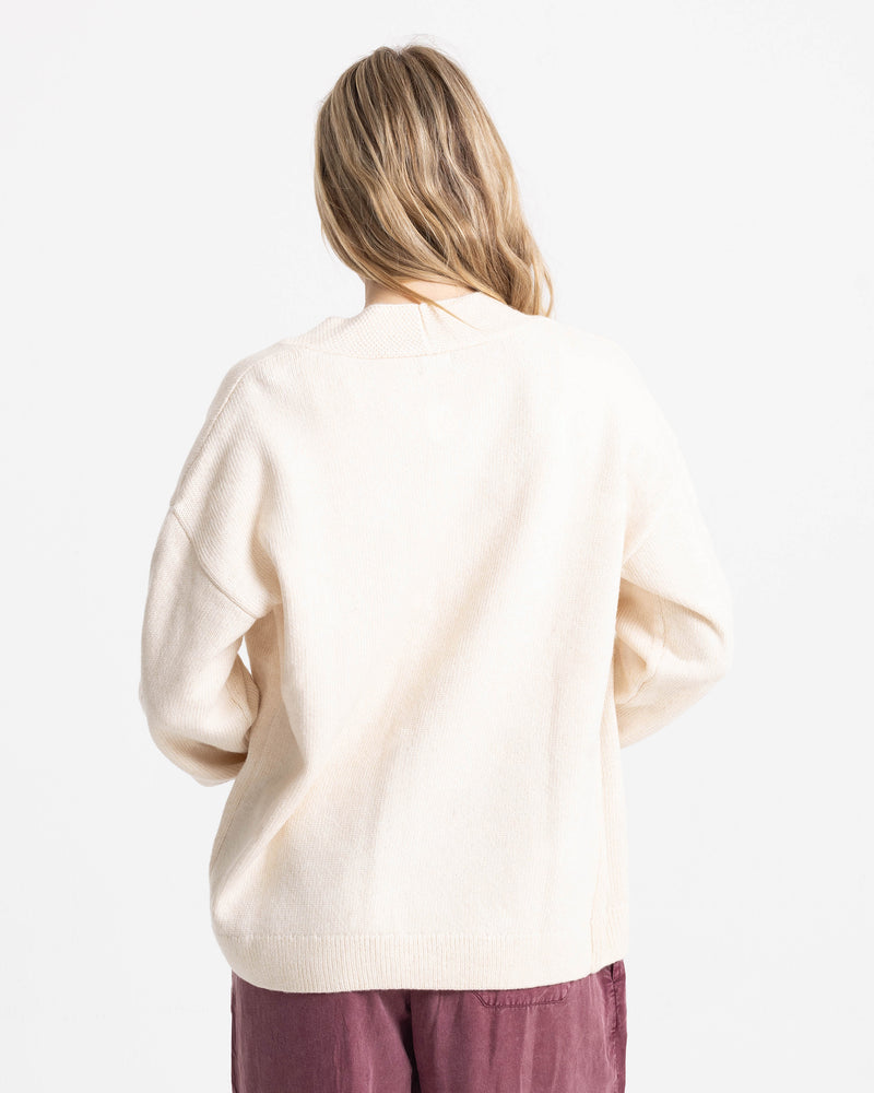 A person seen from the back wearing a cream-colored, cotton-blend Women’s Sweater Weather Cardigan Jacquard and dark red pants.