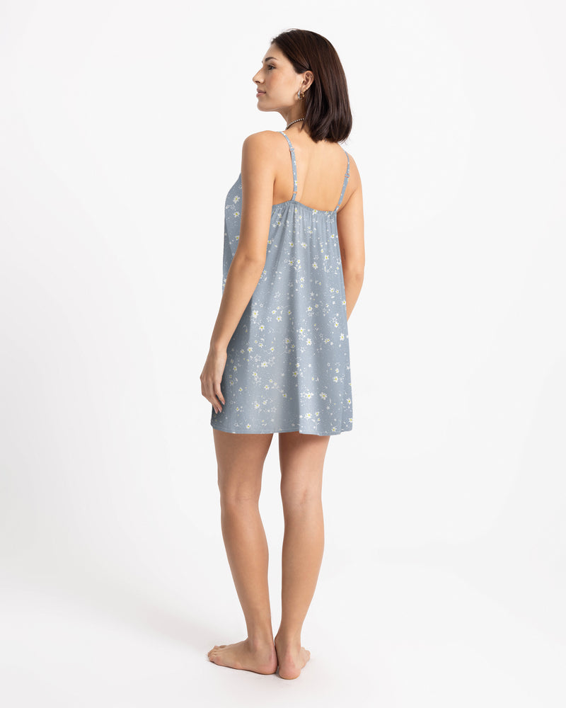 A person seen from the back wears a Women’s Boss Beach Mini Dress by Volcom, a light blue lyocell mini dress with a small white floral print and thin spaghetti straps.