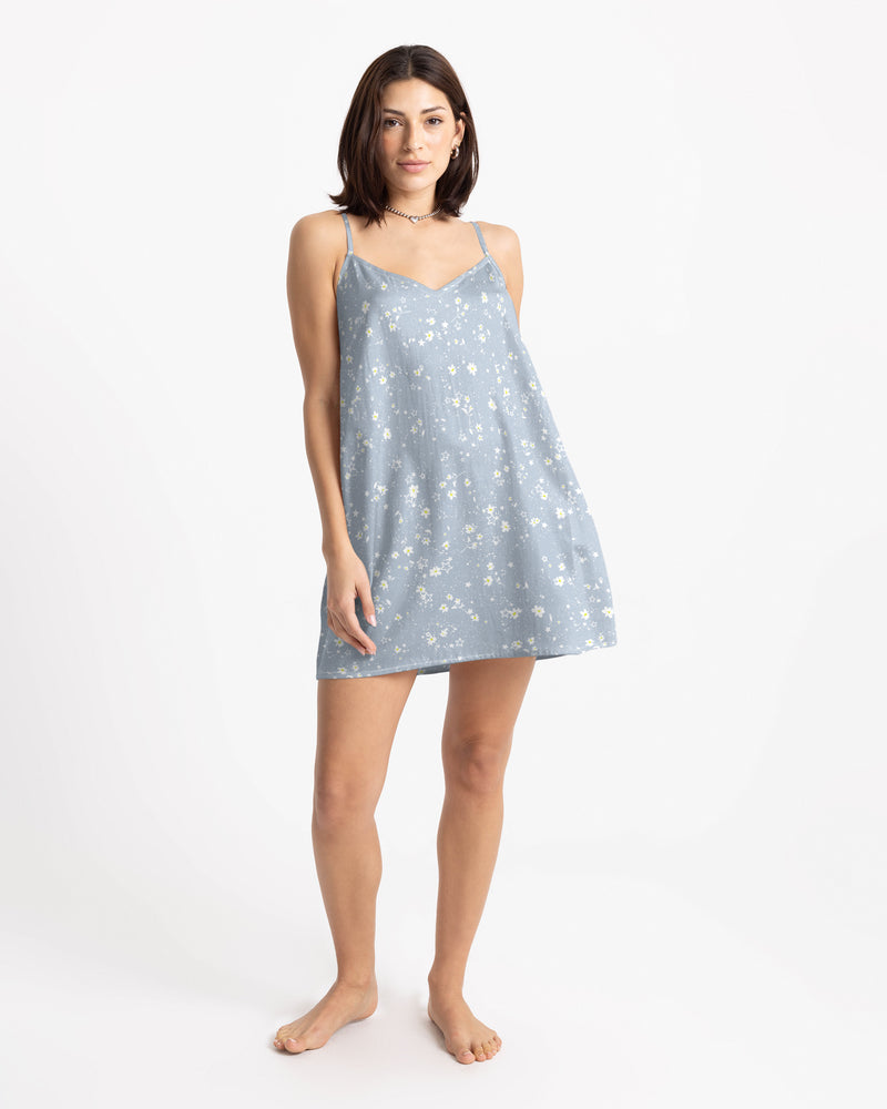 A woman wears a Volcom Women’s Boss Beach Mini Dress in light blue lyocell with a white floral print, thin spaghetti straps, and a simple slip silhouette.