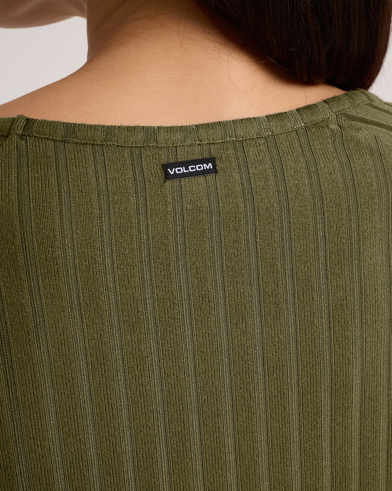 Close-up of the back neckline of an olive green Women’s Sun Lounge Pull Over Long Sleeve with a Volcom tag sewn on. The wearer’s brown hair is partially visible on the right.