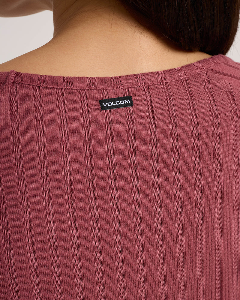 Close-up of the back of a person’s neck wearing a ribbed mauve Women’s Sun Lounge Pull Over Long Sleeve by Volcom, featuring a black brand tag at the neckline.