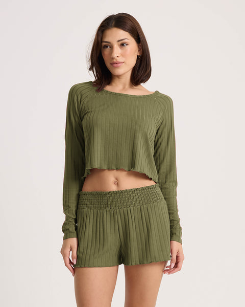 A woman wears a matching Martini Olive ribbed long-sleeve crop top and Volcom Women’s Sun Lounge Short with an elastic waistband, standing against a plain white background.