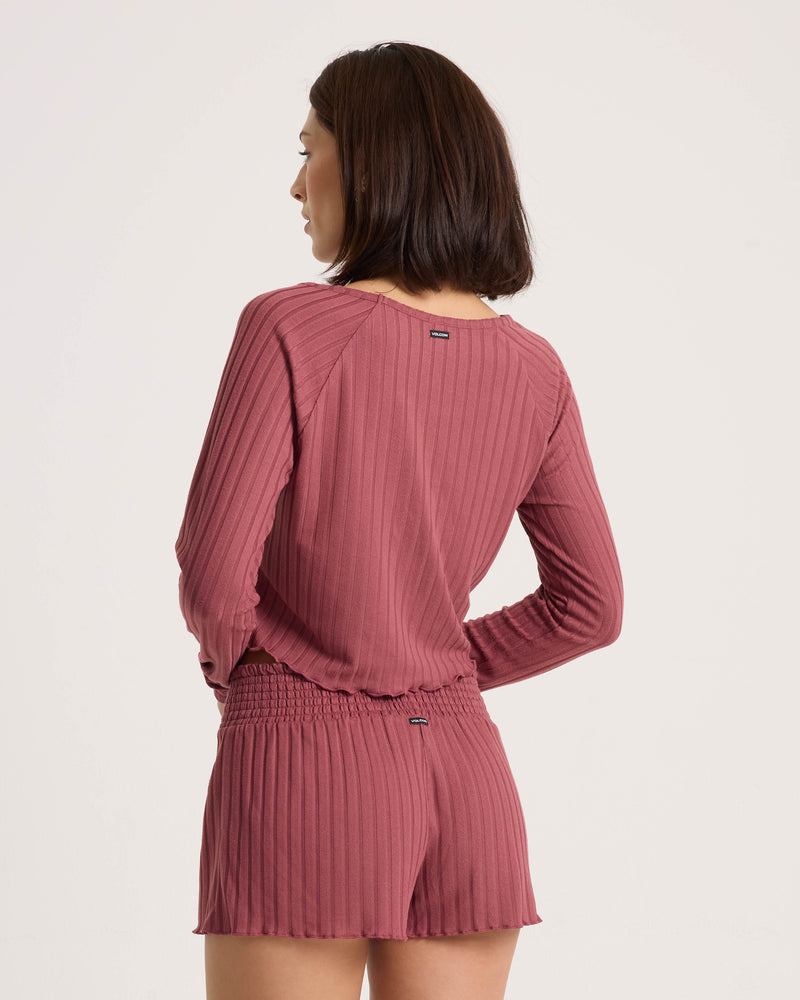 A woman seen from behind wearing a stone rose ribbed long-sleeve top and matching Volcom Women’s Sun Lounge Short with a smocked waistband.