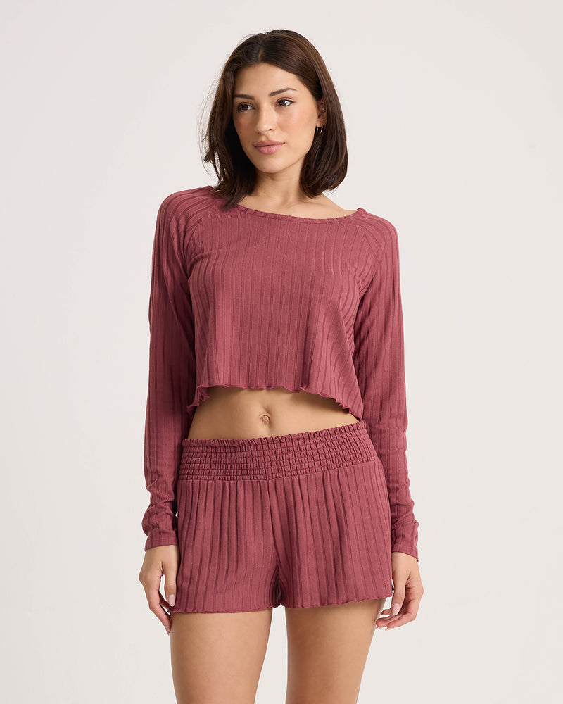 A woman wears a mauve long-sleeve crop top with a lettuce-edge hem and matching Volcom Women’s Sun Lounge Short featuring a relaxed fit and smocked waistband.