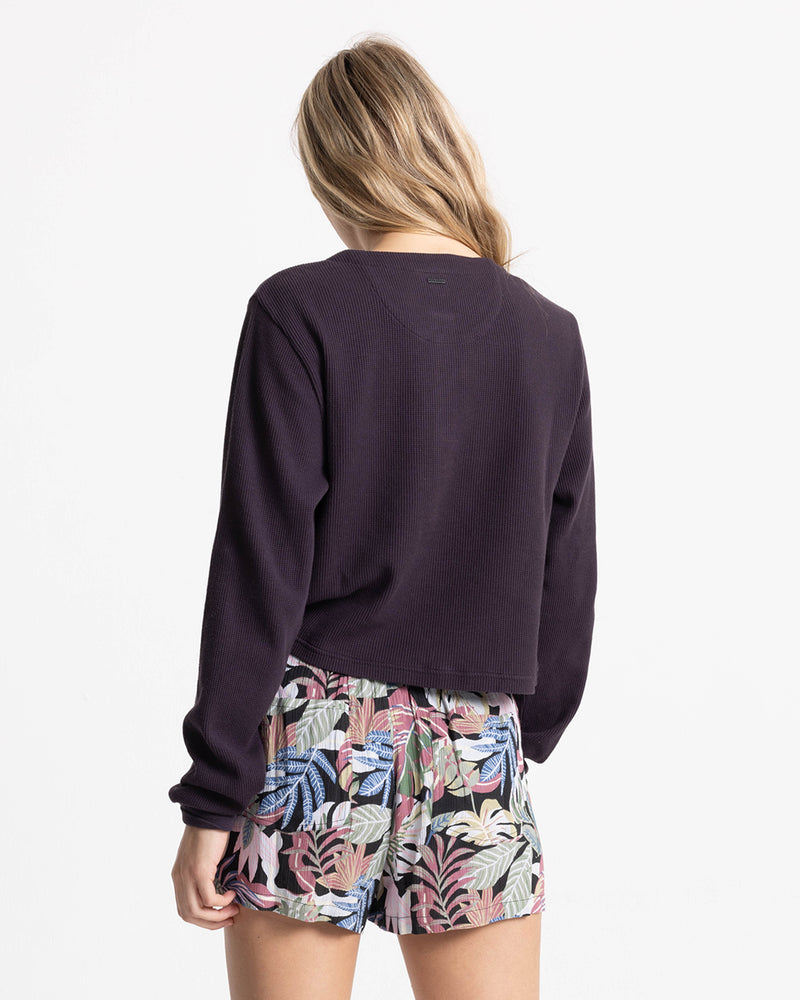 Back view of a person wearing a long-sleeved dark purple waffle-knit shirt and Volcom Women’s Stone Shine Short featuring a colorful tropical Garden Multi leaf print.