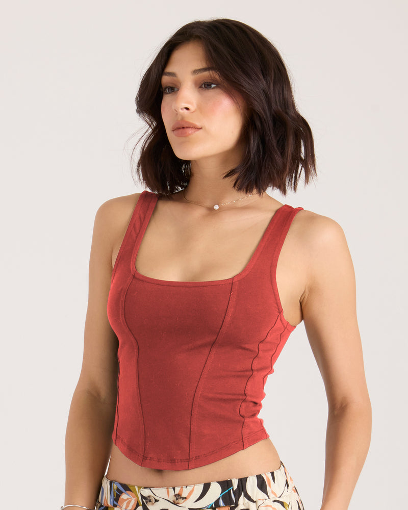 A woman wears a Volcom Women’s Hot Corset Tank in marsala, featuring a square neckline, exposed seams, and a fitted, corset-style knit design.