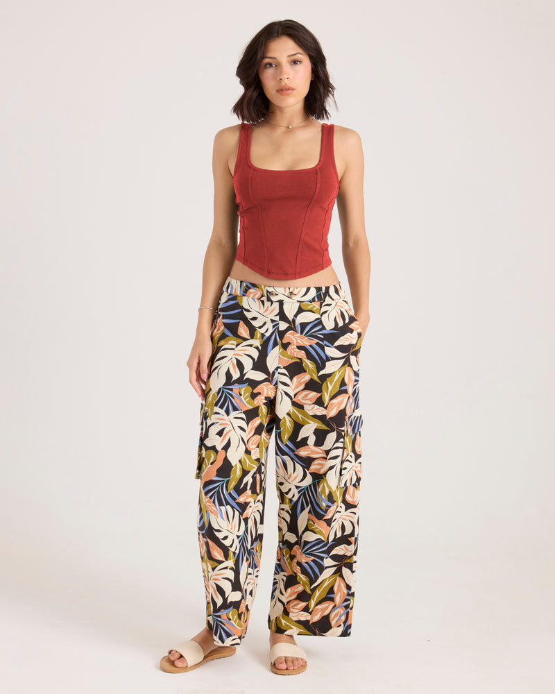 A woman wearing a Marsala Volcom Women’s Hot Corset Tank and wide-leg trousers with a tropical leaf pattern.