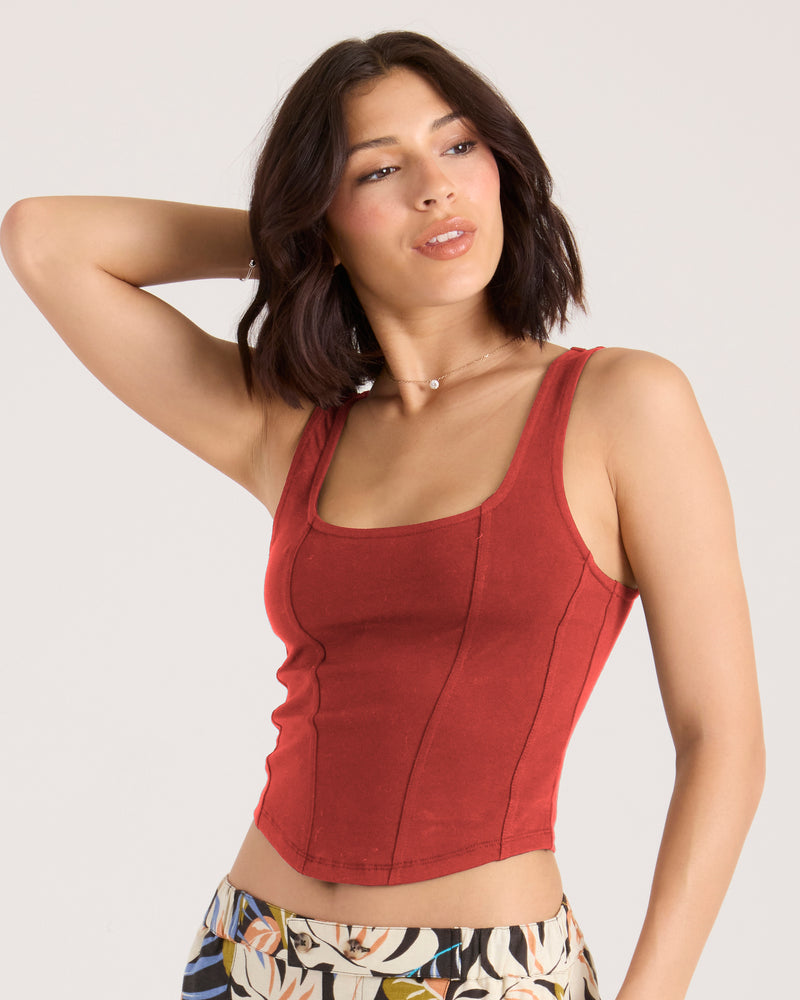 A woman wears a Volcom Women’s Hot Corset Tank in Marsala, featuring a fitted knit design with a square neckline and exposed seam detailing.