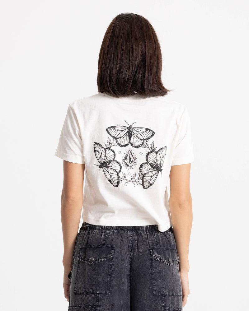 A person facing away wears the Volcom Women’s BuTeeTeeerfly Ring Pocket Dial Tee, featuring a black graphic of four butterflies and a diamond on the back, paired with dark gray cargo pants.