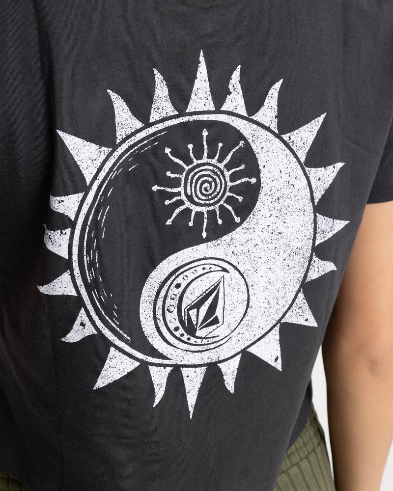 Person wearing the Women’s Ying Yang Pocket Dial Tee by Volcom—a black, soft cotton top with a boxy fit and a white yin-yang design combined with sun rays, a spiral, and abstract geometric patterns.