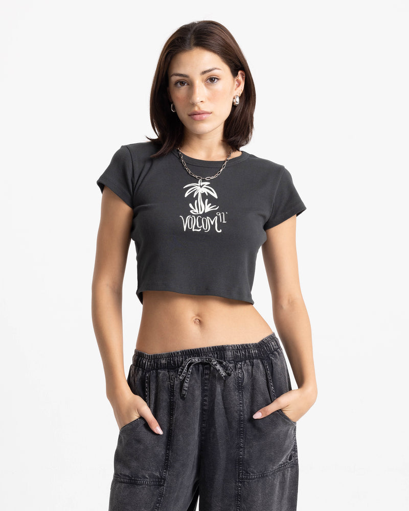 A woman wears a black Women’s Volcom Doodle 1991 Mid Tee, a cropped boxy t-shirt featuring a white palm tree graphic and the text Volcom 91 on the chest.