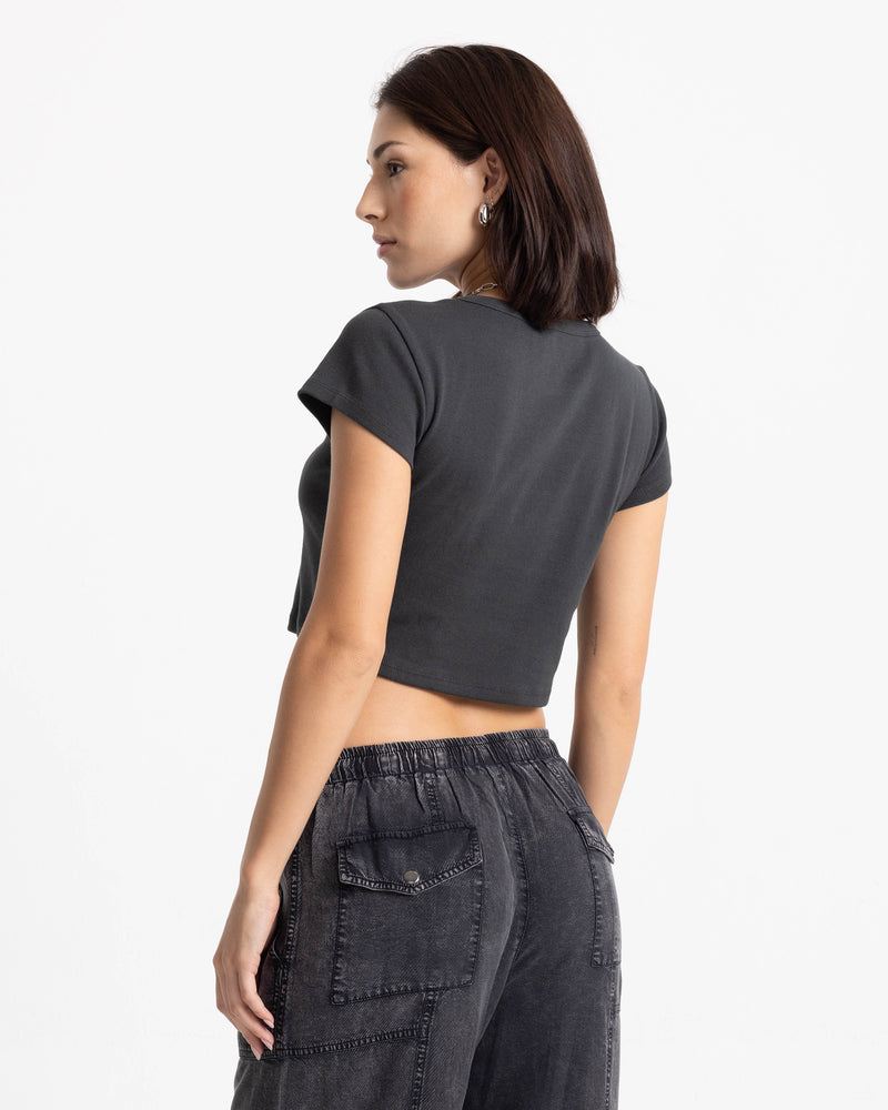 A woman viewed from behind, wearing a charcoal gray Women’s Volcom Doodle 1991 Mid Tee and washed black utility pants.