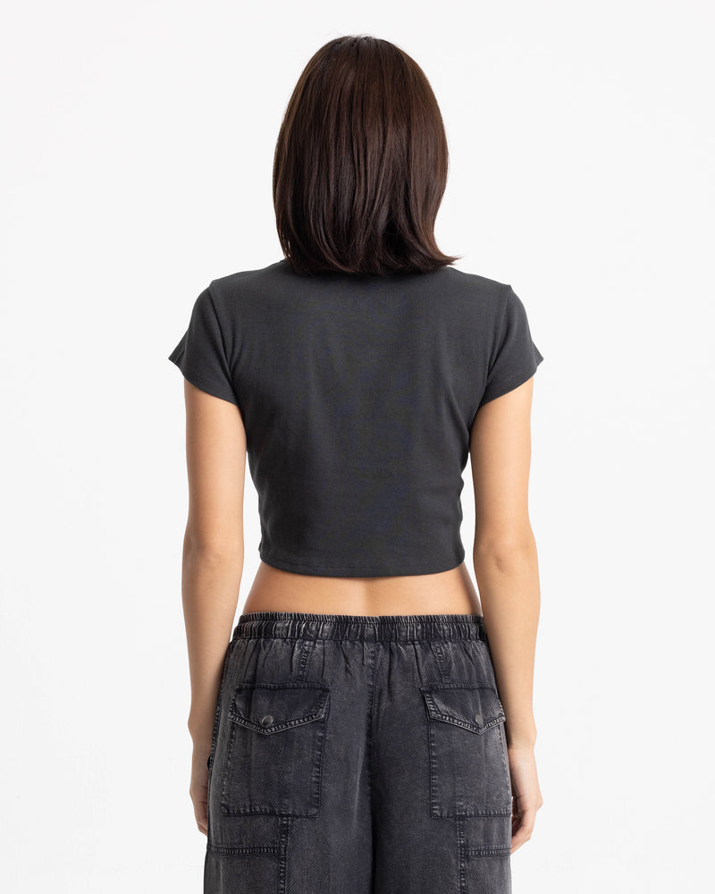 A person seen from the back wearing a charcoal Women’s Volcom Doodle 1991 Mid Tee and charcoal denim pants.