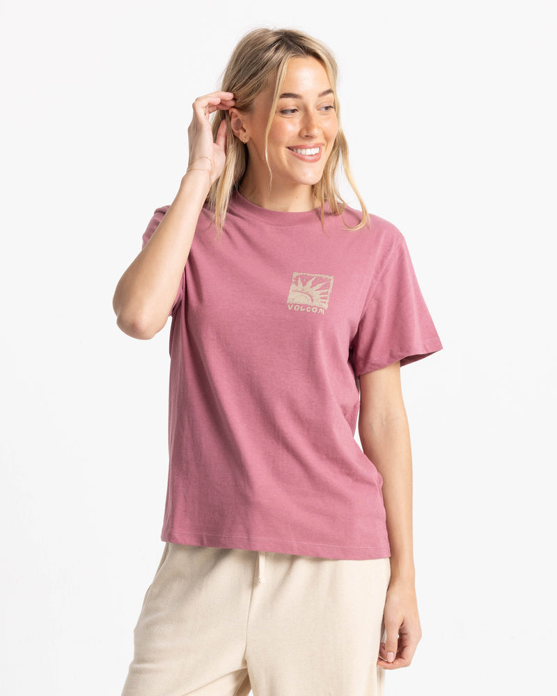 A woman smiling while wearing a dusty pink Women’s Volcom Stamp Lock It Up Tee, featuring a relaxed, boxy fit and a small square graphic on the chest.
