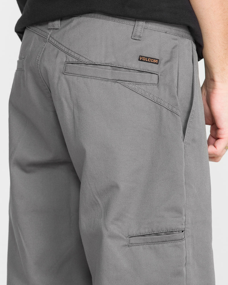 Close-up of a person wearing Men's Frickin Relaxed Chino Pants in gray, featuring back and side pockets and a small Volcom logo label above the right back pocket. The person’s right arm is partially visible.