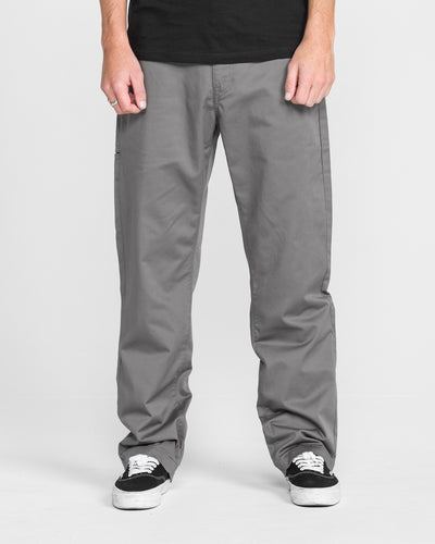 A person wears Men's Frickin Relaxed Chino Pants with black-and-white sneakers, standing against a plain white background. Their hands rest at their sides, and the photo is cropped from the shoulders down.