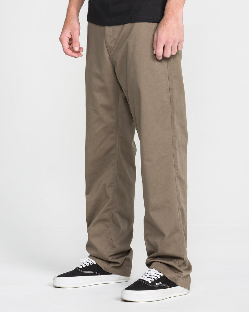 A person wearing Men's Frickin Relaxed Chino Pants stands against a plain white background. The image displays their lower body from the waist down, highlighting the relaxed fit of these khaki pants.