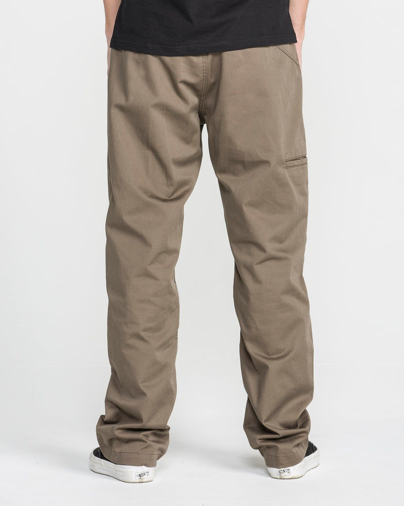 A person wearing Men's Frickin Relaxed Chino Pants and black-and-white sneakers stands with their back to the camera against a plain white background.